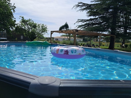 A swimming pool with inflatable toys, surrounded by trees and a wooden pergola.. GITE "les p'tites cagouilles"