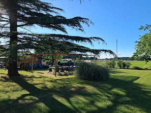Un parque con un pérgola de madera, un área de juegos y una zona cubierta de césped.