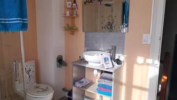 A bathroom with a toilet, sink, and a mirror above the sink. There are shelves with toiletries and a towel hanging on the wall.