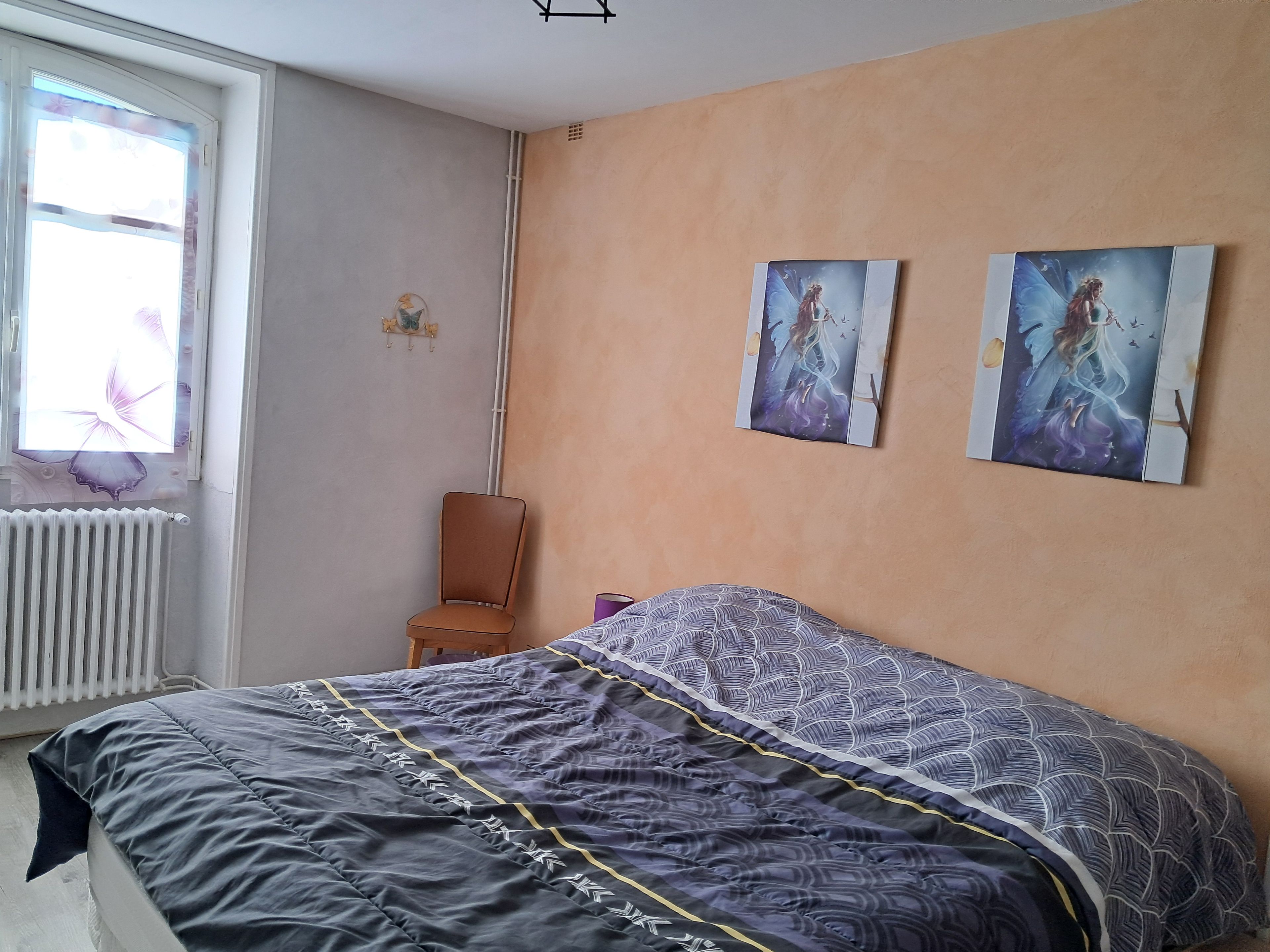A bedroom with a bed, a chair, and two wall-mounted paintings.