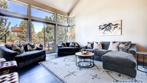 A modern living room with large windows, a sectional sofa, a round coffee table, and a rug with geometric patterns. - Beautiful Eagle Crest Condo, HOT TUB, 2 Bed/2 Bath (Redmond)