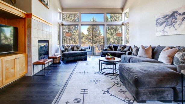A spacious living room with a large TV, comfortable seating, and a view of trees through large windows. - Beautiful Eagle Crest Condo, HOT TUB, 2 Bed/2 Bath (Redmond)