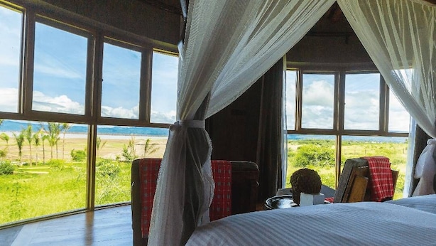 A bedroom with a large window, a bed, and a view of the landscape. - Suricata Boma Lodge (Lake Manyara National Park)