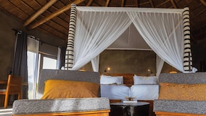 A room with a bed under a canopy, two sofas with cushions, a small round table, and a wooden floor. - Suricata Boma Lodge (Lake Manyara National Park)