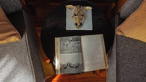 A book with a zebra illustration and text on a table, placed in a wooden cabin with upholstered chairs. - Suricata Boma Lodge (Lake Manyara National Park)