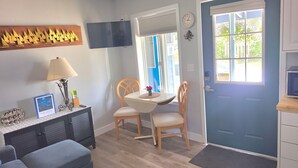 A compact living space with a dining area, a television mounted on the wall, a door with a window, and a small kitchenette. - Blue Octopus #2 Beach Access (Rockaway Beach)