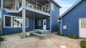 A two-story house with a balcony, a front door, and a concrete patio with a picnic table. - Blue Octopus #2 Beach Access (Rockaway Beach)