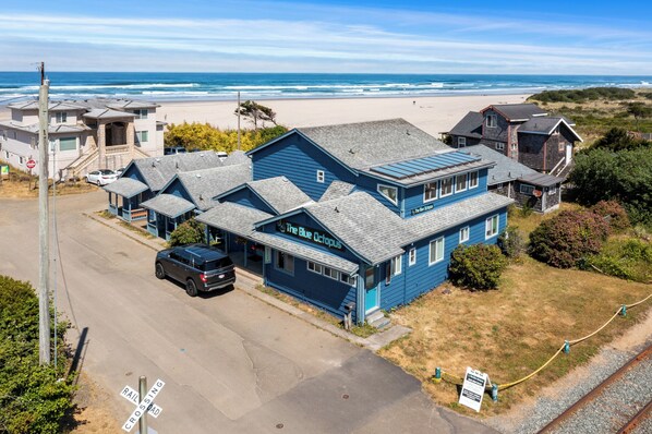 A coastal hotel with a prominent blue building named "The Blue Octopus," situated near a beach and railroad crossing. - Blue Octopus #2 Beach Access (Rockaway Beach)