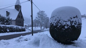 A snow-covered spherical sculpture in a residential area with a church and a road. - Chez Jacotte (Gérardmer)