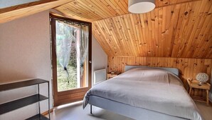 A bedroom with a sloped ceiling, a bed, a bedside table, a lamp, and a window with curtains. - Chez Jacotte (Gérardmer)