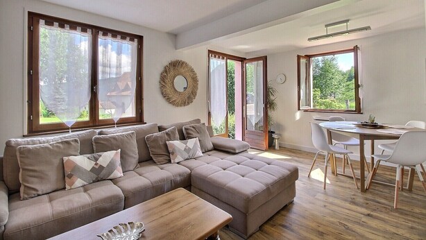 A modern living room with a sectional sofa, a wooden coffee table, and a dining area with a table and chairs. - Chez Jacotte (Gérardmer)