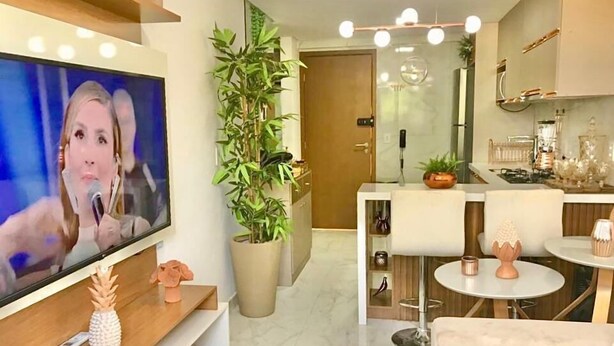 Uma sala de estar moderna com televisão, um vaso de planta e uma área de jantar com mesa redonda e cadeiras.