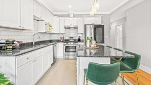 A modern kitchen with white cabinets, a granite countertop, stainless steel appliances, and green upholstered bar stools.