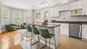 A modern kitchen with white cabinets, a stainless steel dishwasher, and a central island with bar stools.