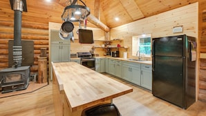 Une cuisine rustique, située dans une cabane en bois, avec un îlot central, une cuisinière, des placards et un réfrigérateur.
