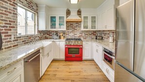 A kitchen with white cabinets, a red oven, stainless steel appliances, and a brick wall. - Luxe 3BR Executive Home w/ Pool, Office & Patio (Las Vegas)