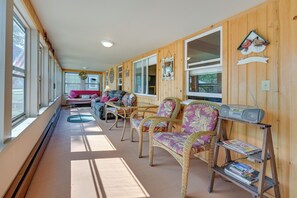 A sunlit room with wicker furniture, a table, and a shelf with books. - 4-Season Anglers Cabin At Shawano Lake w/ Views! (Shawano)