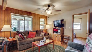 A living room with a sofa, armchair, coffee table, TV, and a ceiling fan. - 4-Season Anglers Cabin At Shawano Lake w/ Views! (Shawano)