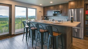 A modern kitchen with a large island, bar stools, a stainless steel refrigerator, and a view of the countryside. - Steamboat Springs Apt w/ Views, 15 Mi to Skiing! (Steamboat Springs)