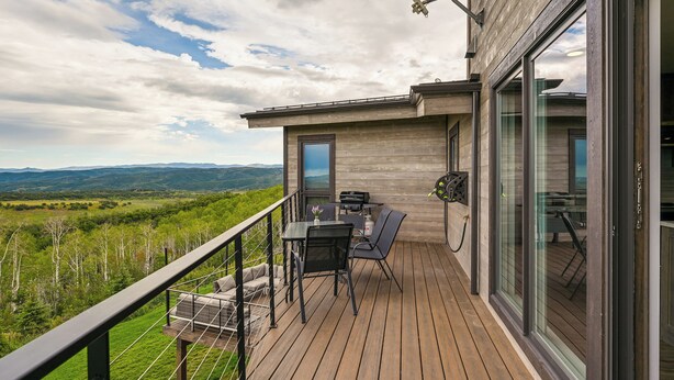 A wooden deck with outdoor furniture, a glass door, and a view of the landscape. - Steamboat Springs Apt w/ Views, 15 Mi to Skiing! (Steamboat Springs)