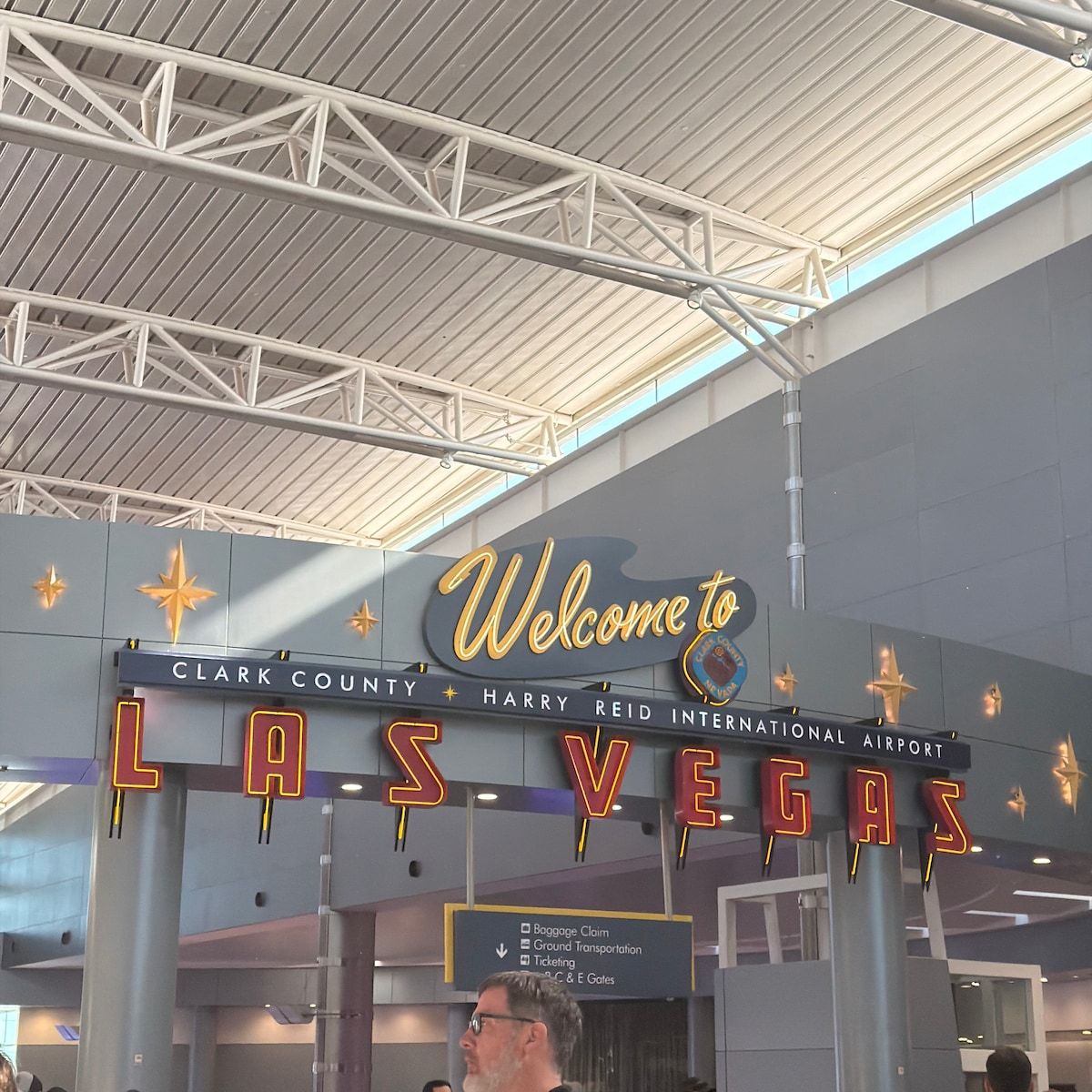 A sign at an airport entrance with 'Welcome to LAS VEGAS' and 'CLARK COUNTY HARRY REID INTERNATIONAL AIRPORT' text.