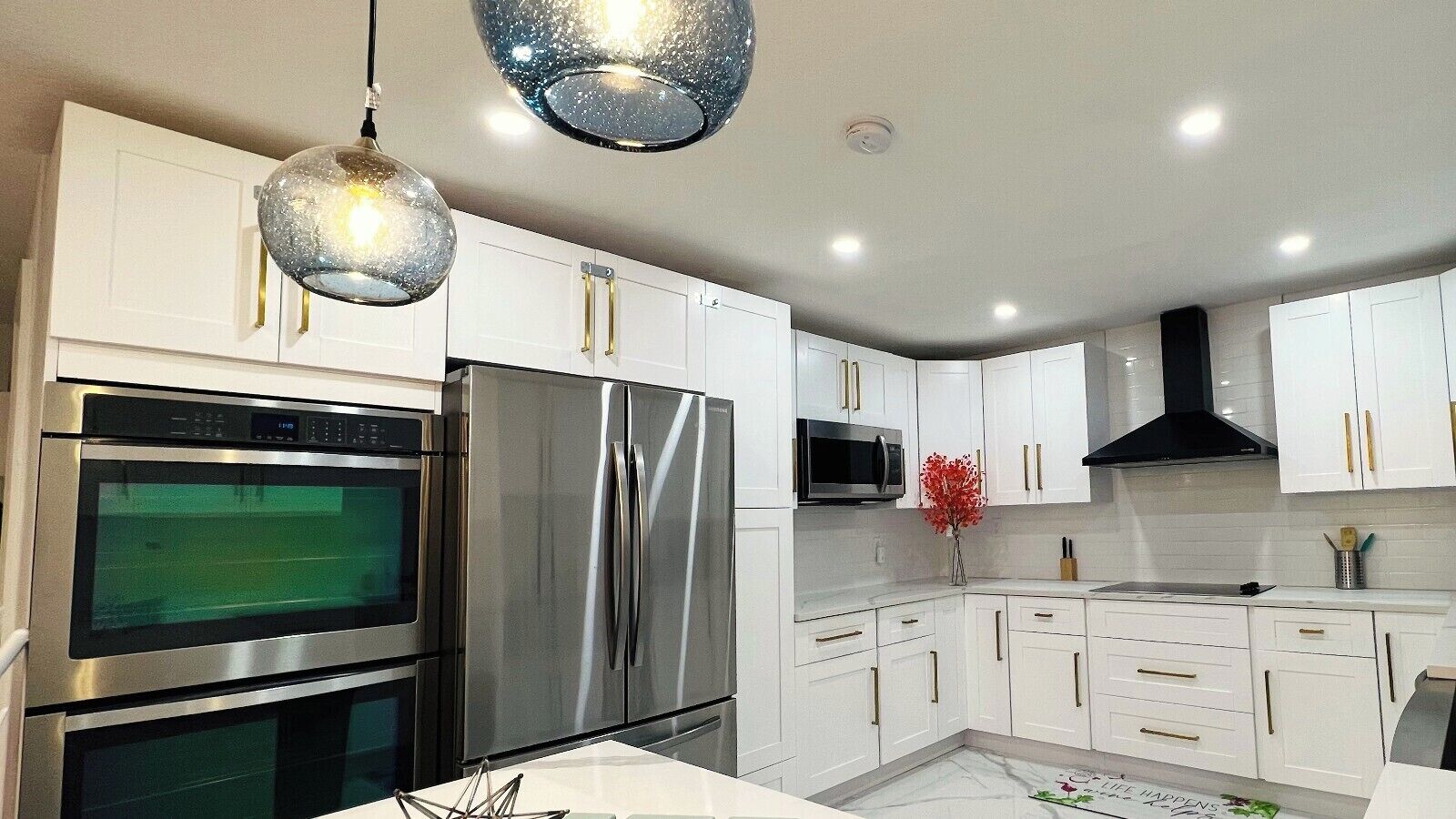 A modern kitchen with stainless steel appliances, white cabinetry, and pendant lighting.