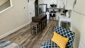 A compact kitchen with white cabinets, a refrigerator, microwave, and stove. There is a wooden dining table with two chairs and a small rug on the floor. - Downtown retreat by the Bay, Bruce Beach, Blue Angels,  parades & fish market!  (Pensacola)