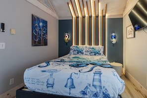 Une chambre à coucher avec un lit agrémenté d’une couette aux motifs marins, un luminaire fixé au mur et un tableau encadré.