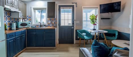 Una cocina compacta con comedor, un televisor montado en la pared y una puerta que da a otra habitación.