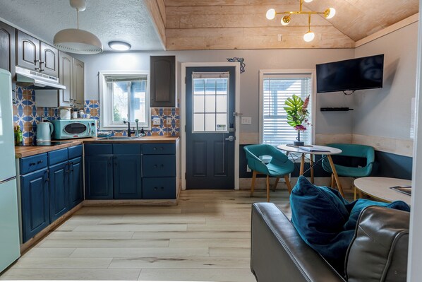 A compact kitchen with a dining area, a television mounted on the wall, and a door leading to another room.
