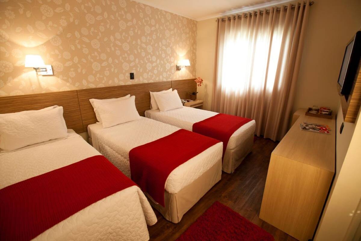 A hotel room with three beds, a wooden headboard, a desk, and a television.