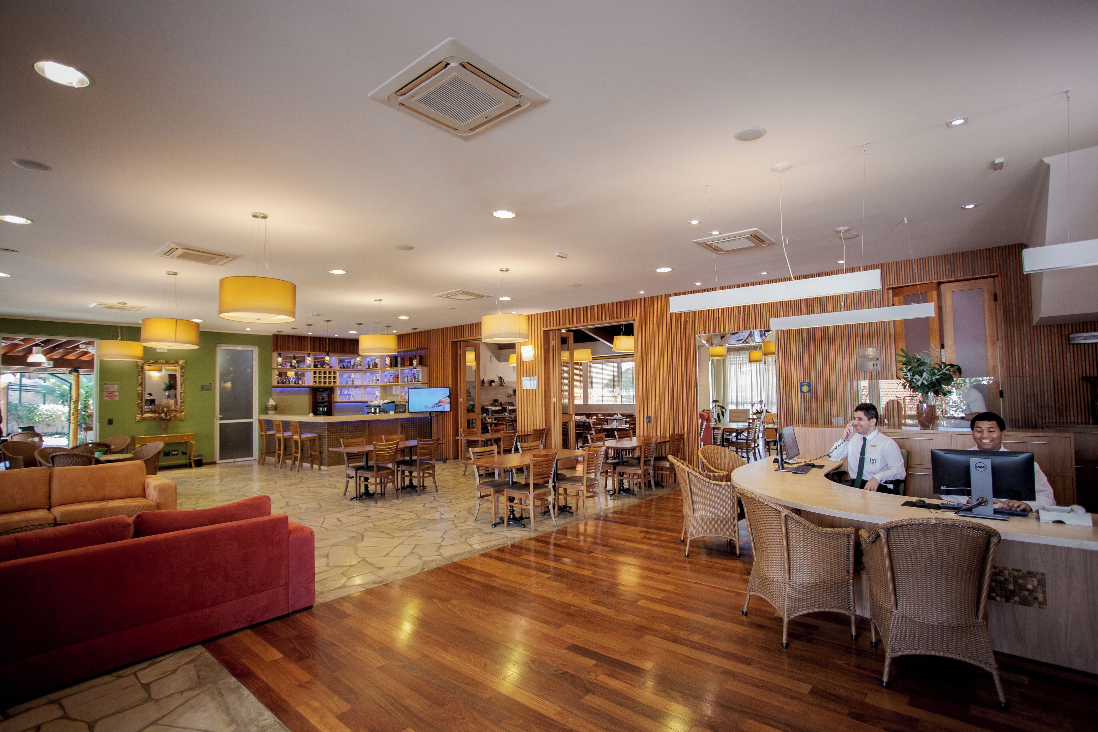 Um hall amplo com balcão de atendimento em madeira, assentos confortáveis e um espaço para bar.