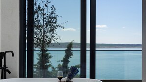 Un bagno moderno con vasca, cabina doccia in vetro e vista su un corpo d'acqua e alberi.