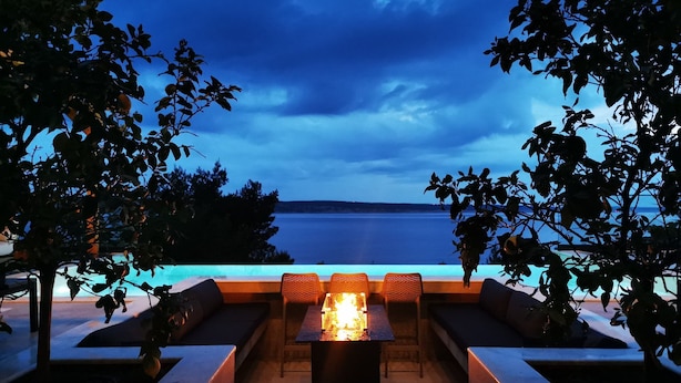 Area salotto esterna con un elemento decorativo a fuoco, con vista su uno specchio d'acqua.