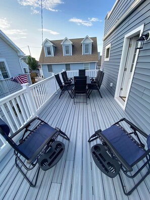 A wooden deck with a table and chairs, a white railing, and a view of a house with a brown roof.