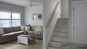 Ein Wohnzimmer mit Ecksofa, Couchtisch und einer Treppe mit hölzernem Geländer.