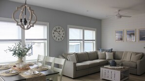Ein Wohnzimmer mit Esstisch für vier Personen, einem beigefarbenen Sofa, einem Couchtisch und einer Kronleuchter.