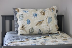 A bed with a quilted bedspread featuring a nautical theme, a pillow with a similar pattern, and a dark wooden headboard.