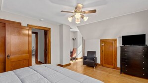 A bedroom with a large bed, a ceiling fan, a TV, and a dresser. - The Lewis & Clark Hangout (Saint Charles)