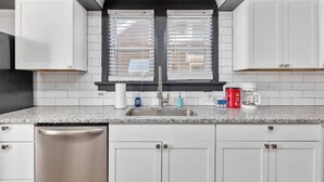 A kitchen with white cabinets, a stainless steel sink, and a window with blinds. - The Lewis & Clark Hangout (Saint Charles)