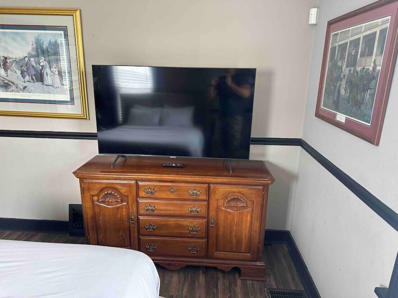 A hotel room with a wooden dresser, a flat-screen TV, and two framed pictures on the walls.