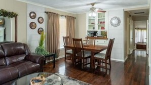 A living room with a leather sofa, a glass coffee table, and a dining area with wooden chairs and a table. - Cozy & Cheerful 4 Bedroom Home Near Downtown (Fort Smith)