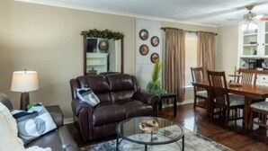 A living room with a leather sofa, a glass coffee table, a dining table with chairs, and a fireplace. - Cozy & Cheerful 4 Bedroom Home Near Downtown (Fort Smith)