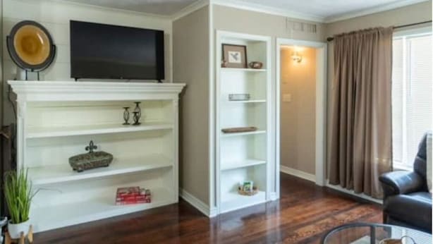 A living room with a fireplace, a flat-screen TV mounted above it, and a bookshelf. - Cozy & Cheerful 4 Bedroom Home Near Downtown (Fort Smith)