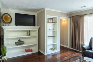 Een woonkamer met een open haard, een flatscreen televisie erboven en een boekenkast.