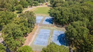 An aerial view of a tennis court surrounded by dense trees. - Cozy & Cheerful 4 Bedroom Home Near Downtown (Fort Smith)