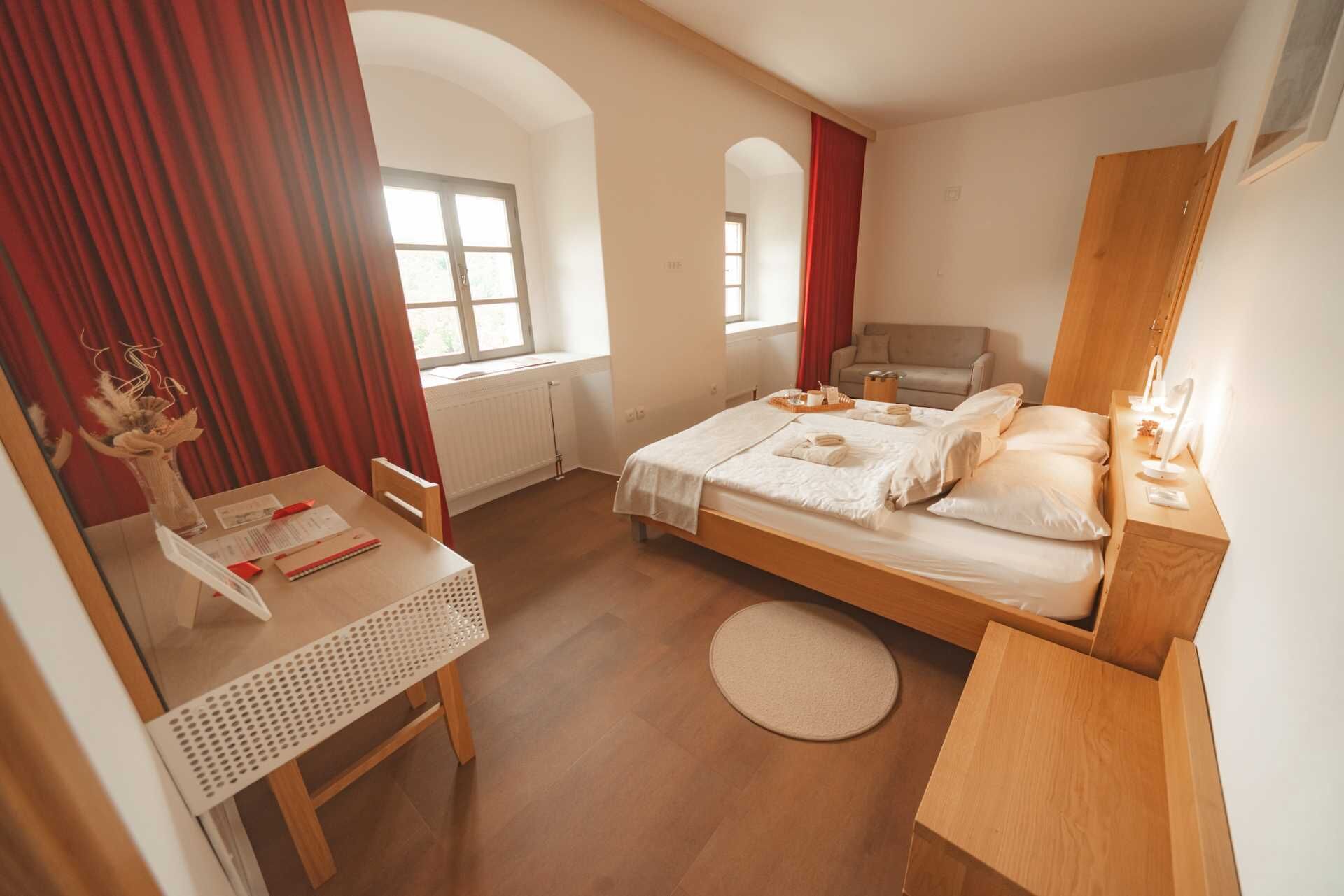 A bedroom with a bed, a desk, a chair, a window, and a mirror.