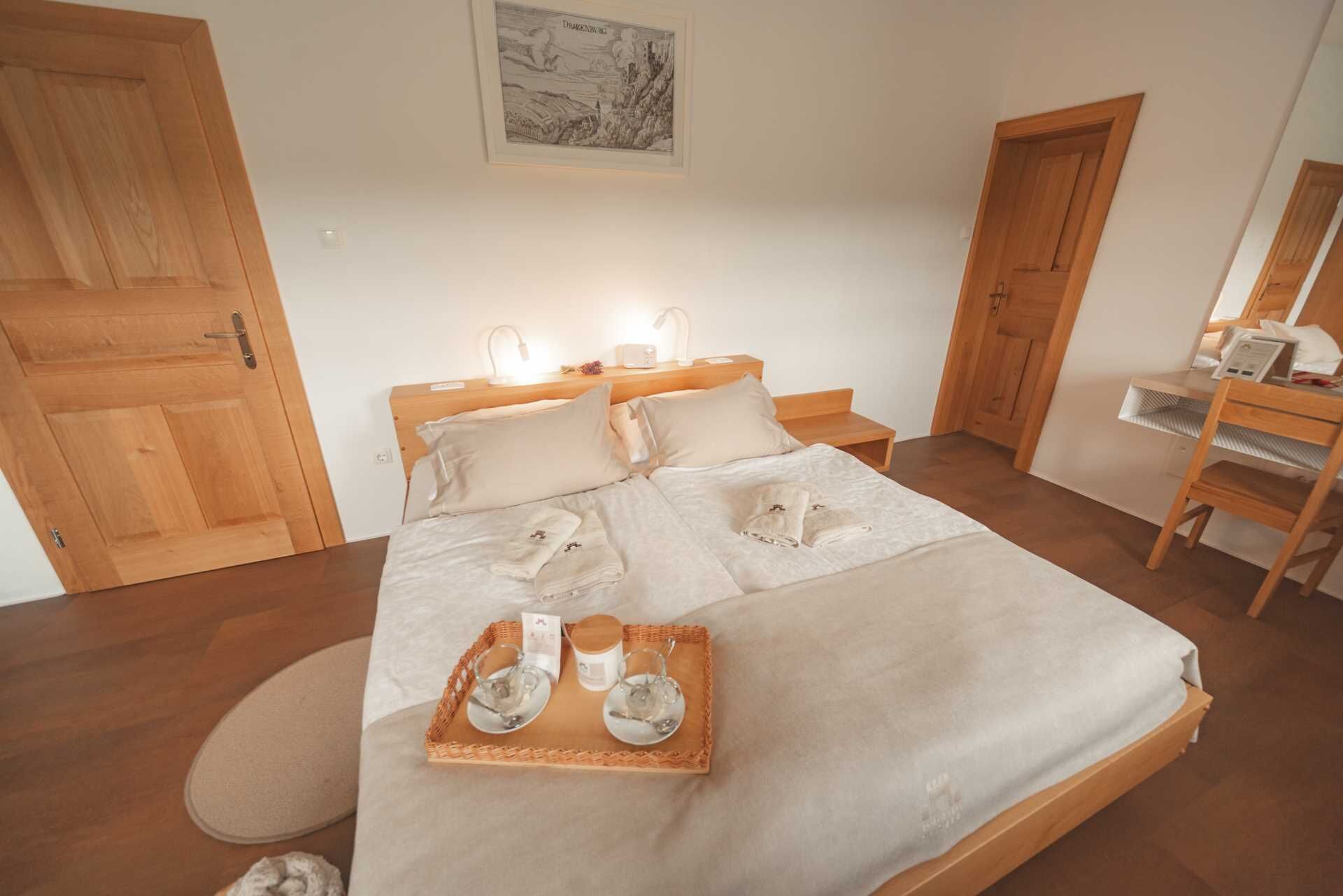 Un letto rifatto con cura, un vassoio con asciugamani e bicchieri, mobili in legno e un quadro appeso alla parete.