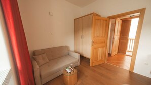 Une pièce comprenant un canapé, une table basse en verre, une armoire en bois et une porte donnant sur une autre pièce.