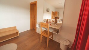 Une petite pièce bien rangée, avec un bureau en bois, une chaise, une petite table, un banc, une poubelle et une porte.